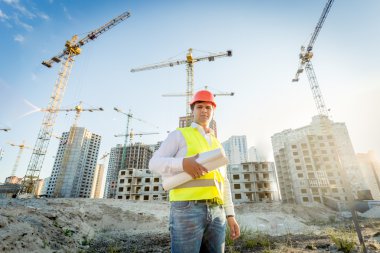 construction inspector posing with blueprints on building site