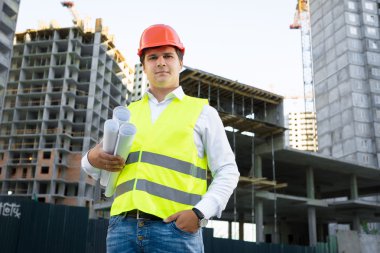 site manager posing with blueprints against unfinished building