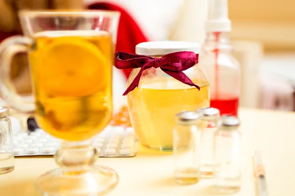 Closeup of hot tea, honey jar and pills on bedside table — Stockfoto