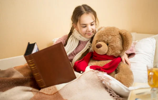 Portrait of brunette girl telling story to teddy bear at bed — 图库照片