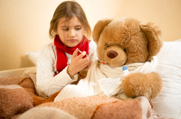 Girl playing and measuring teddy's bear temperature with thermom — Stockfoto