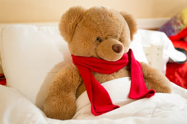 Closeup of brown teddy bear in red scarf lying in bed — 스톡 사진