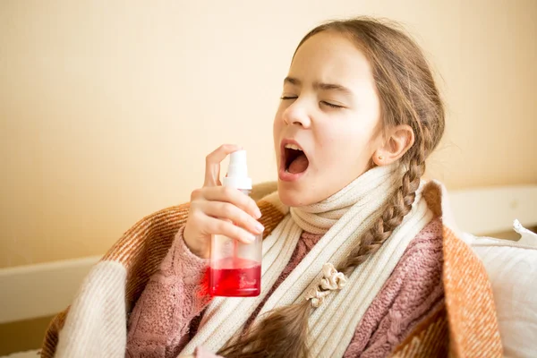 Sick girl covering in blanket using throat spray — Stockfoto