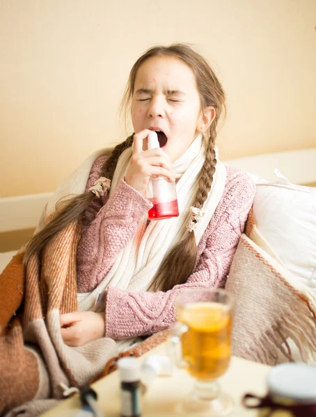 Chica enferma acostada en la cama y usando aerosol de garganta — Foto de Stock