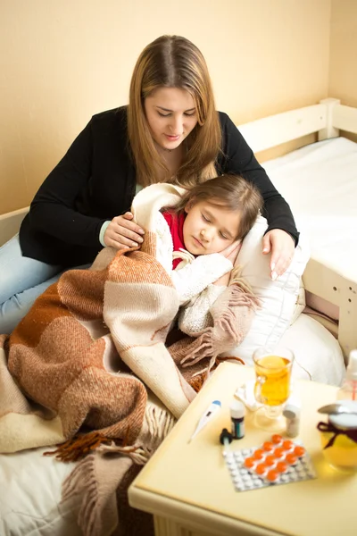 Portrait of caring mother hugging sick girl lying in bed — Zdjęcie stockowe