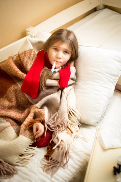 Sick girl lying in bed with teddy bear and measuring temperature — 스톡 사진