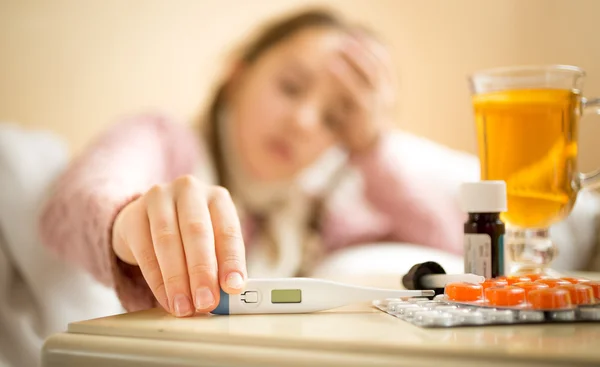 Sick girl taking digital thermometer from bedside table — Stockfoto