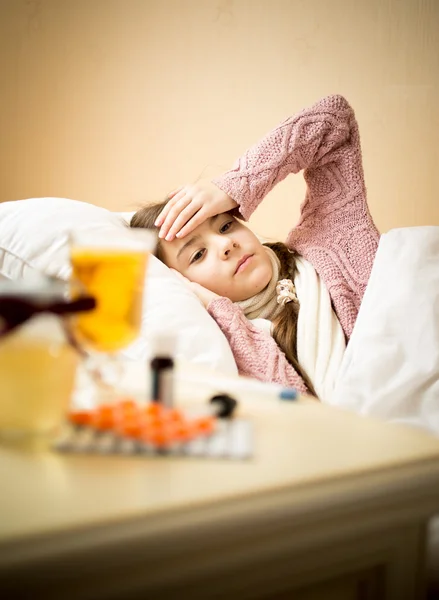 Chica enferma acostada en la cama al lado de la mesa con medicamentos —  Fotos de Stock