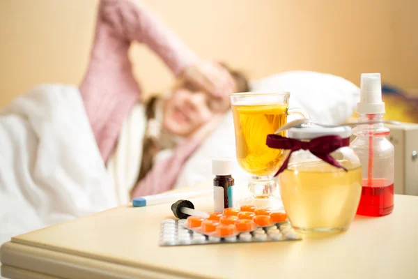 Jar with honey and medicines lying on table next to sick girl be — ストック写真