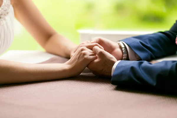 Closeup of bride and groom holding hands on table at restaurant — Stock fotografie