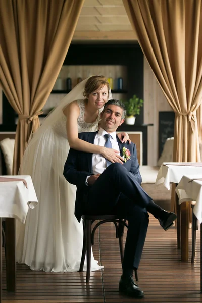 Smiling bride hugging groom from back at restaurant — Stock Photo, Image