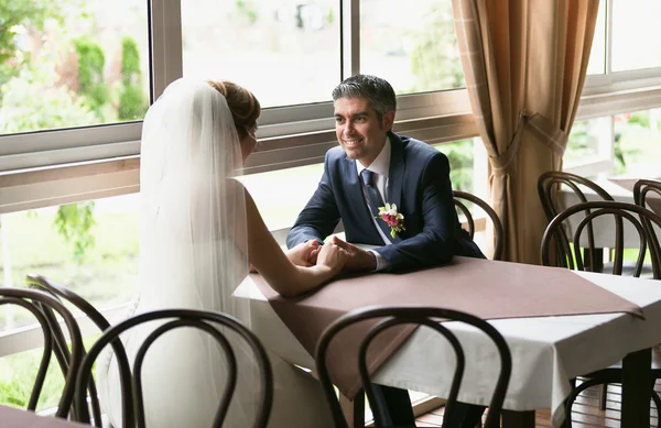 Smiling groom and bride sitting at table in restaurant — Stok fotoğraf