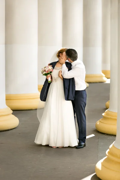 Groom covering brides shoulders with jacket and kissing her — Stock Photo, Image