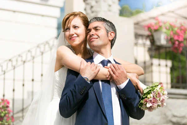 Beautiful bride hugging grooms shoulders on street at sunny day — Stock Photo, Image