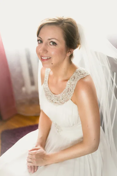 Elegante novia sonriente posando en la silla en el dormitorio — Foto de Stock