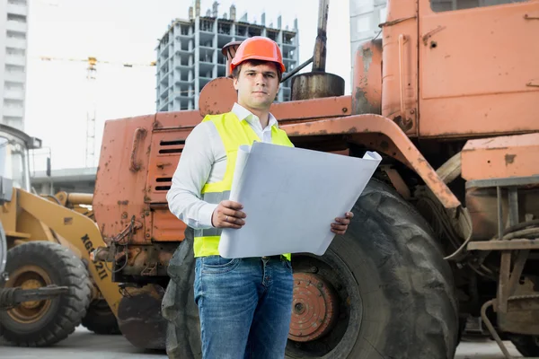 Architect reading blueprints next to bulldozer at building site — 스톡 사진