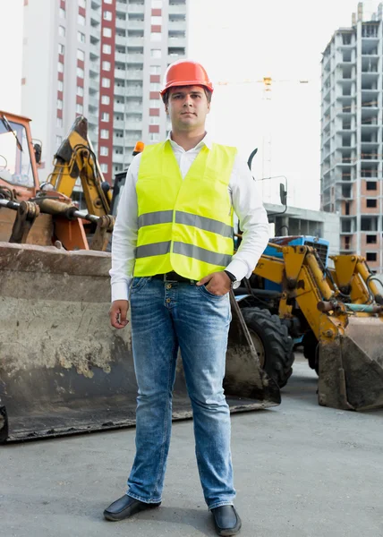 Businessman in safety jacket and hardhat posing next to bulldoze — Stock Photo, Image