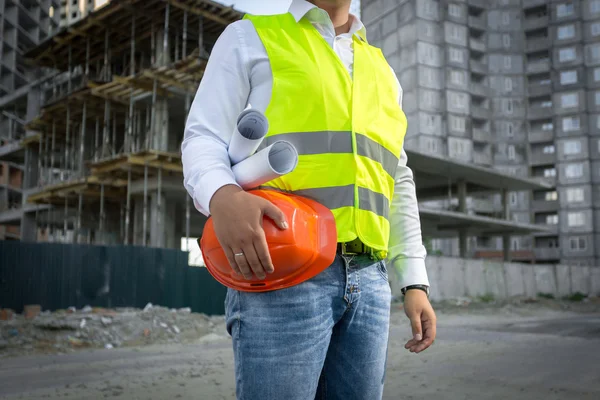 Architect in jacket posing with red helmet at construction site — 스톡 사진