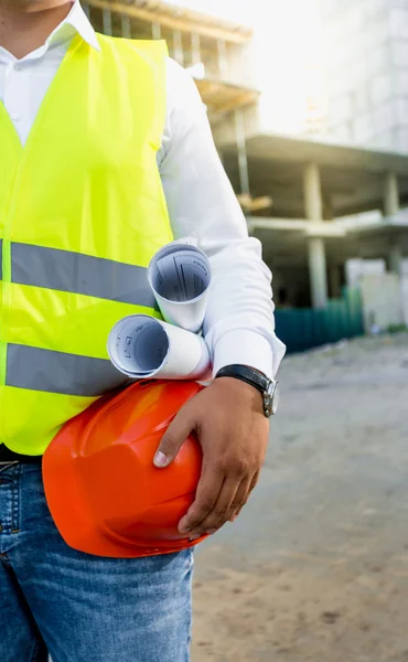 Architect posing on building site with hardhat and blueprints — Stockfoto