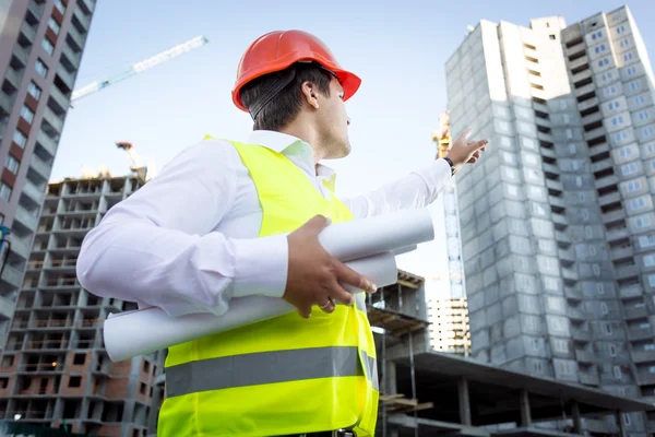 Porträt eines Vorarbeiters mit Bauplänen, die Hand auf Gebäude zeigen — Stockfoto