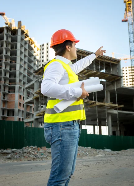 engineer in hardhat and safety jacket checking building site 
