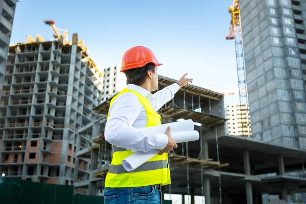 manager in hardhat pointing at crane on building site