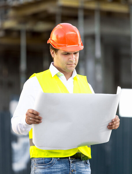 foreman reading blueprints against scaffolding at building site