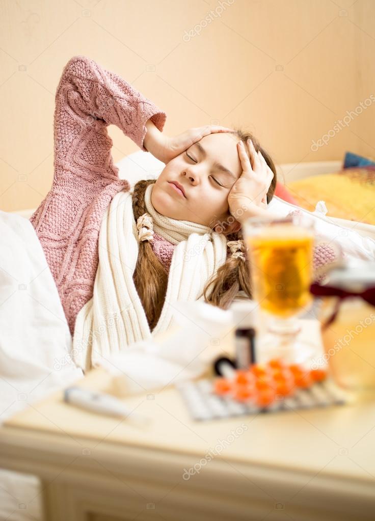 girl with flu lying in bed and holding hands on head