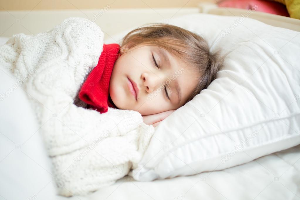 portrait of cute girl in sweater and scarf lying on white pillow