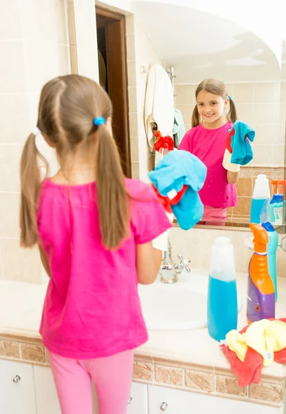 Kleines Mädchen poliert Spiegel im Badezimmer mit Reinigungsmittel — Stockfoto