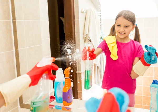 Menina sorrindo espelho de limpeza no banheiro com spray e pano — Fotografia de Stock