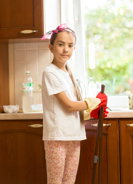 Sorridente ragazza posa sulla cucina disordinata con scopa e paletta — Foto Stock