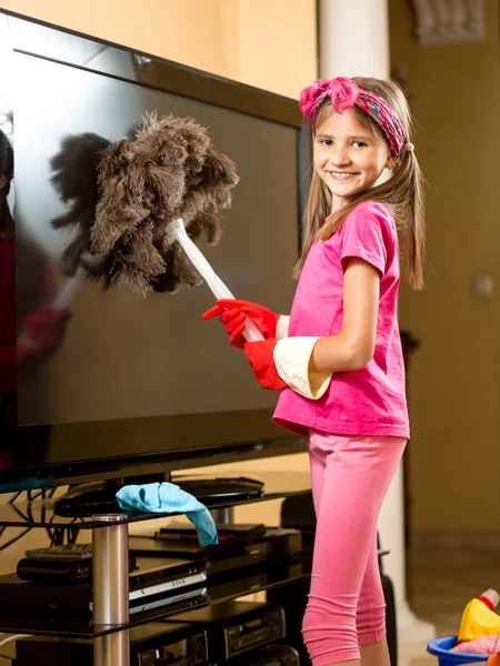 Nettes lächelndes Mädchen, das den Fernseher im Wohnzimmer von Staub befreit — Stockfoto