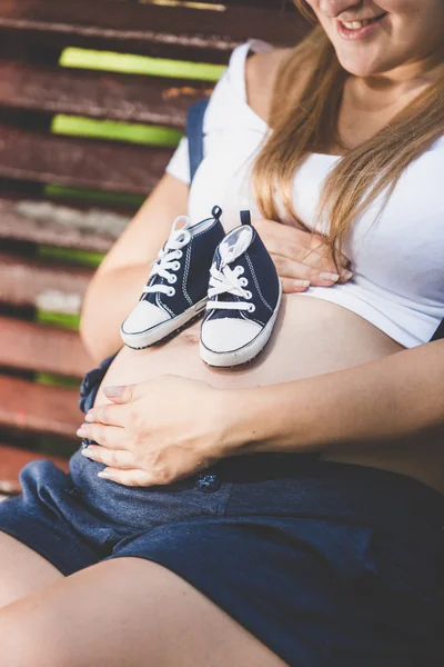 Toned photo of baby shoes on female pregnant abdomen — Stock Photo, Image