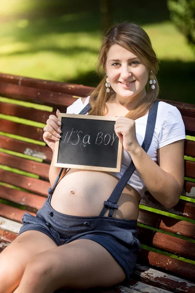 Mujer embarazada sonriente sosteniendo pizarra con texto "Es un niño " — Foto de Stock