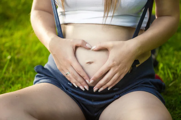 Zorg van zwangere vrouw hand in hand in hart vorm op buik — Stockfoto