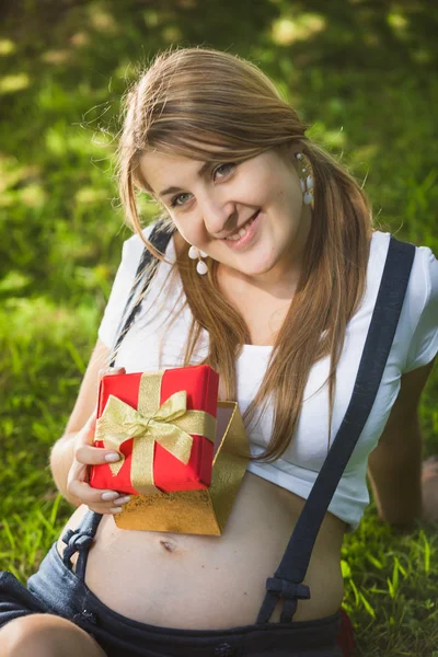Retrato de mulher grávida sorridente posando com caixa de presente no parque — Fotografia de Stock