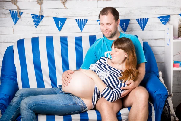 Jovem casal grávida deitado no sofá e olhando para o grande abdômen — Fotografia de Stock