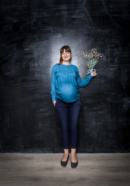 Happy těhotná žena pózuje s kyticí na velké tabuli — Stock fotografie