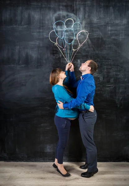 Pregnant couple flying up on the balloons drawn on chalkboard — Stock Photo, Image