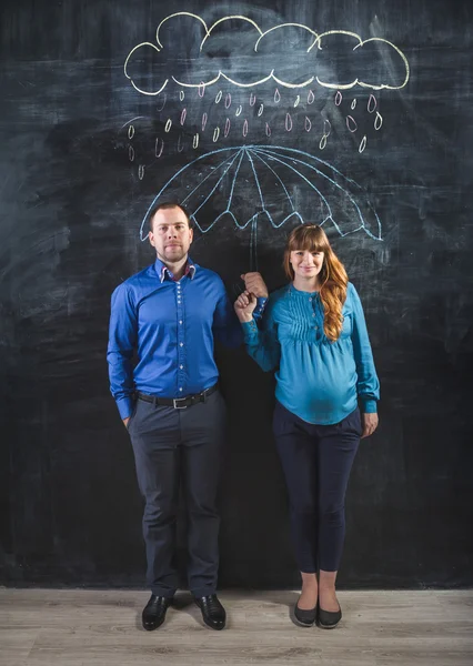 Pregnant woman and man covering under umbrella drawn on blackboa — Stock Photo, Image