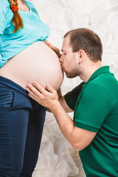 Handsome man kissing pregnant wife at big tummy — Stock Photo, Image