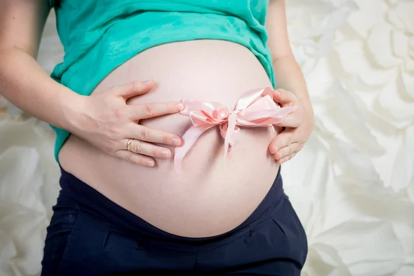 Primo piano della donna incinta in posa con fiocco rosa sulla pancia — Foto Stock