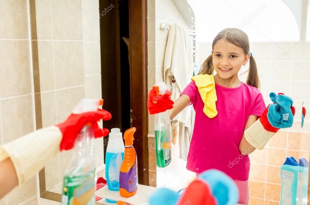 happy smiling girl polishing mirror at bathroom with cloth