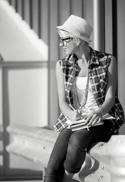 Portrait of stylish girl in eyeglasses and hat writing in notebo — Stock Photo, Image