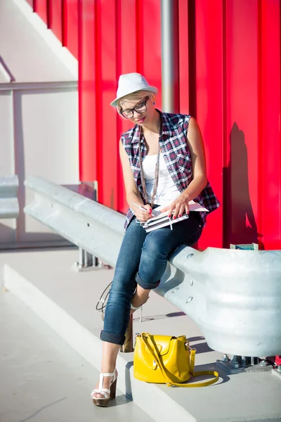 Chica con estilo en jeans y sombrero sentado en la calle y libro de lectura — Foto de Stock