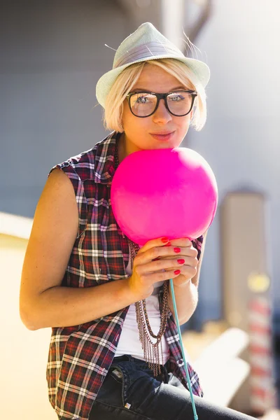 Hipster girl in hat and eyeglasses posing with pink balloon — Stock Photo, Image