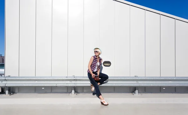 Hipster girl sitting on steel protection fence on parking — Stock Photo, Image