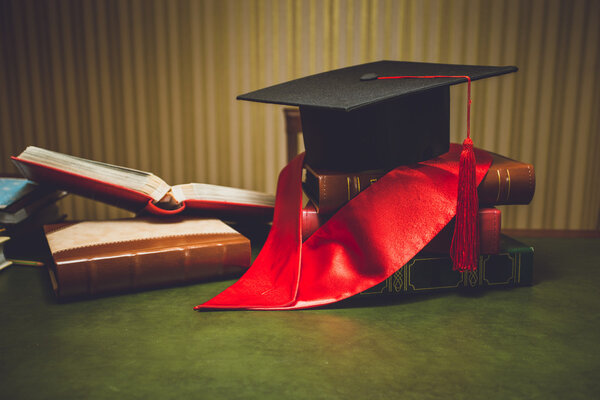 Toned photo of red ribbon and graduation cap on classic table
