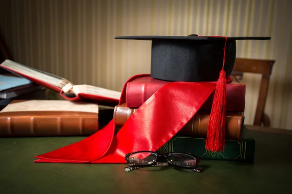 Avläggande av examen cap och rött band liggande på böcker på biblioteket — Stockfoto